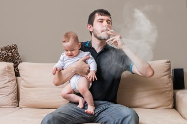 Bad father is smoking and holding baby. A lot of smoke around. clipart