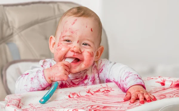 Messy and dirty baby is eating from spoon. — Stock Photo, Image