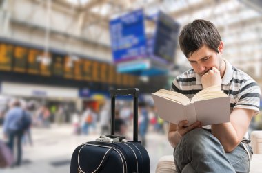 Gecikmeli tren kavramı. Yolcu tren istasyonunda, kitap okuma ve tren varış için bekleyen oturuyor.