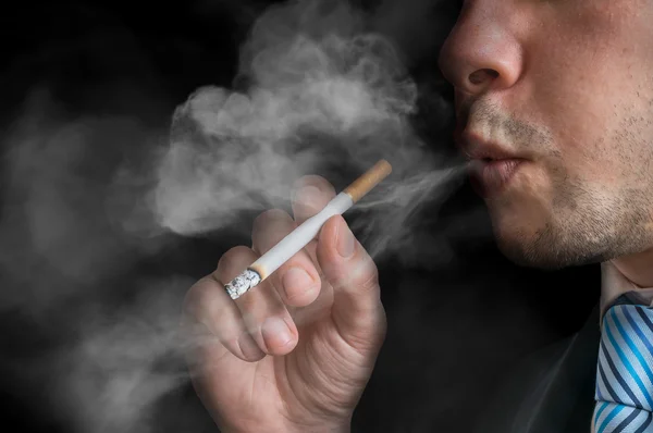 Jovem (fumante) segura cigarro e fumo. Há muito fumo por aí. Foto chave baixa . — Fotografia de Stock
