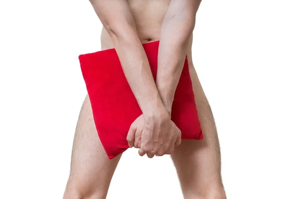 Ashamed young naked man is covering his penis with red pillow. — Stock Photo, Image