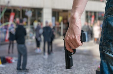 Silahlı adam (saldırgan) tabanca halka açık bir yerde tutar. Birçok kişi sokakta. Silah kontrolü kavramı.
