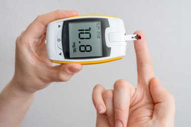 Diabetic patient is holding glocimeter and measuring glucose level in blood. clipart