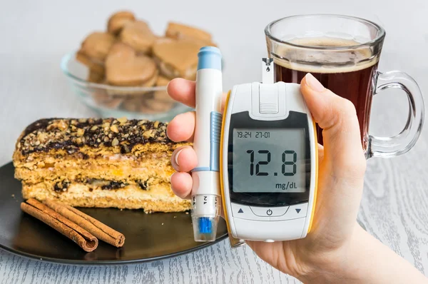 Diabetes and unhealthy eating concept. Hand holds glucometer and sweets and cake in background. — Stock Photo, Image