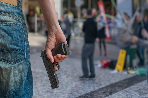 Koncepcja sterowania pistoletu. Uzbrojony człowiek-napastnik trzyma pistolet w ręku w miejscu publicznym. Wiele osób na ulicy. — Zdjęcie stockowe