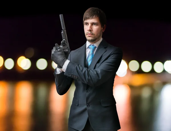 Killer of Assassin houdt pistool met geluiddemper in handen 's nachts. Vage lichten op de achtergrond. — Stockfoto