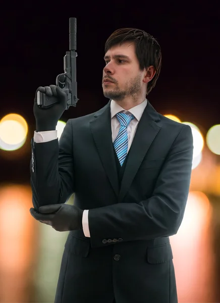 Secret agent in suit holds pistol with silencer in hand at night