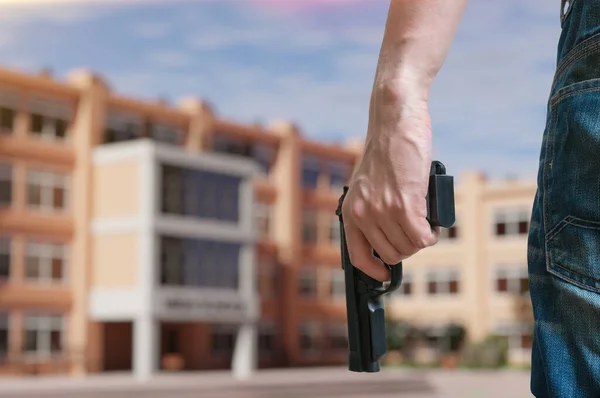 Young armed man holds pistol in hand in public place near high school. Gun control concept.