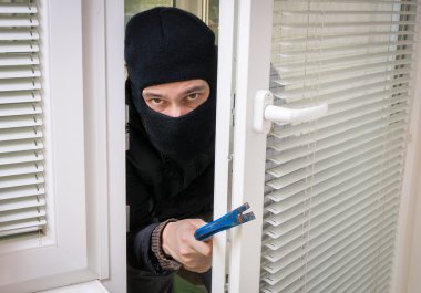 Masked robber or thief with balaclava is opening door with crowb clipart