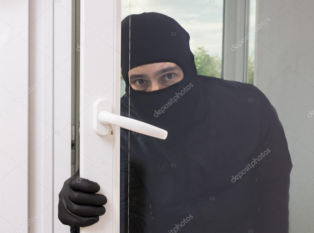 Masked thief or burglar in black balaclava is opening door or wi