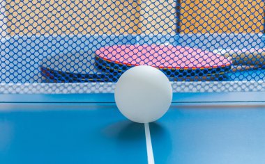 Ping pong topu ve raketleri net arkasında.