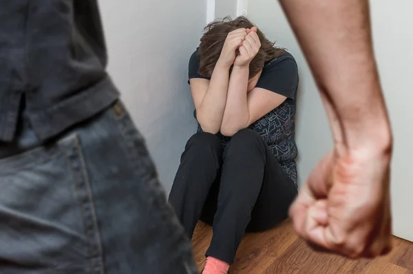 Кулак разъяренного мужчины и плачущая женщина сидят в углу. Концепция домашнего насилия — стоковое фото