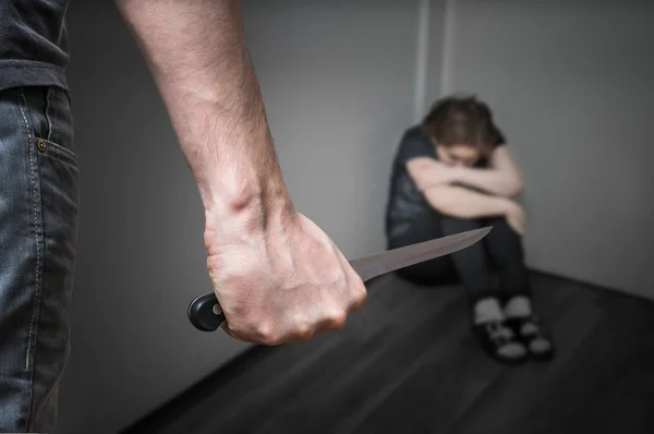 Domestic violence concept. Woman sitting in corner and is scared of man with knife — Stock Photo, Image