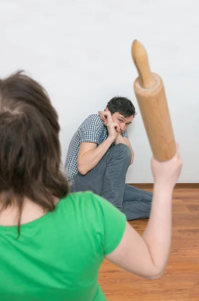 Wife is attacking her henpecked husband with a roller pin. Domestic violence concept — Stock Photo, Image