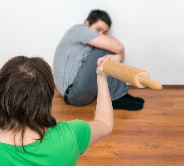 Dominant woman is attacking her henpecked scared husband with a roller pin. — Stock Photo, Image