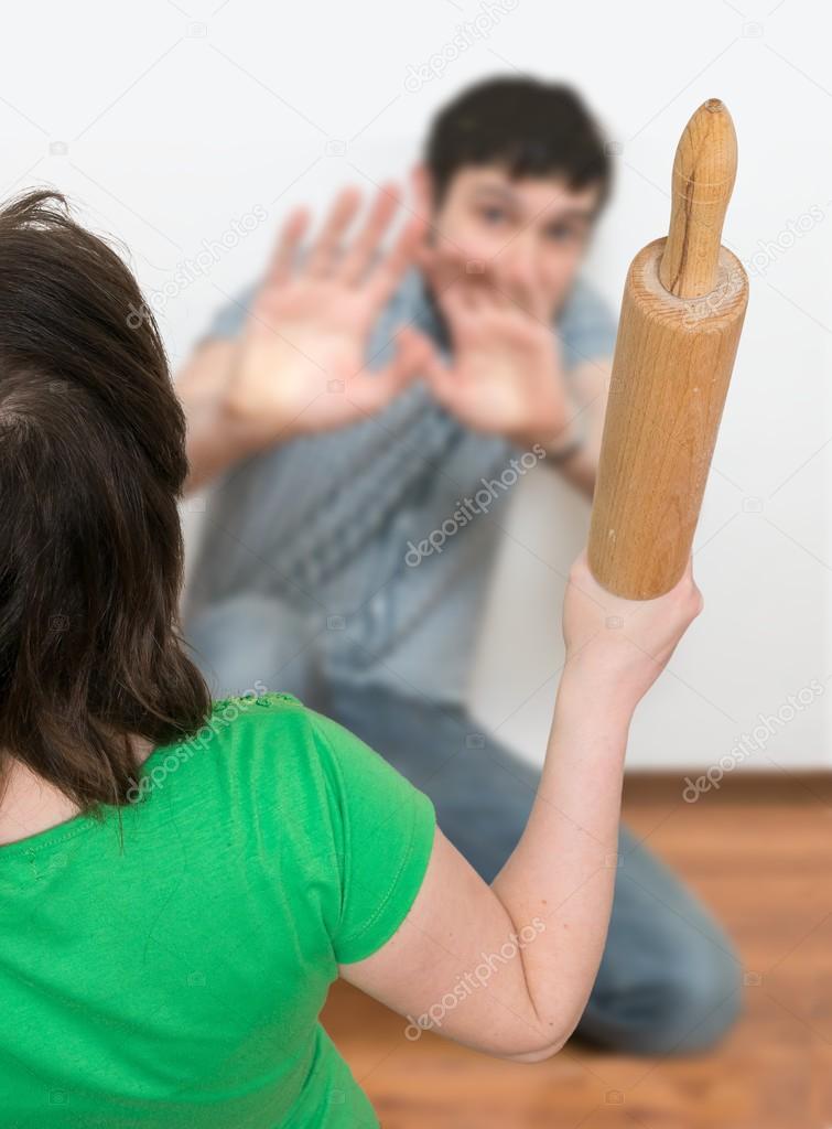 Angry woman is attacking henpecked man with a roller pin. Divorce concept.