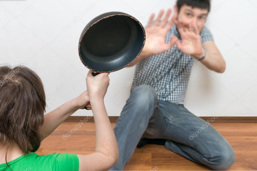 Wife is attacking her husband with a frying pan. Domestic violence concept.