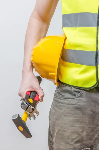 Obrero sostiene casco amarillo, martillo y otras herramientas . — Foto de Stock