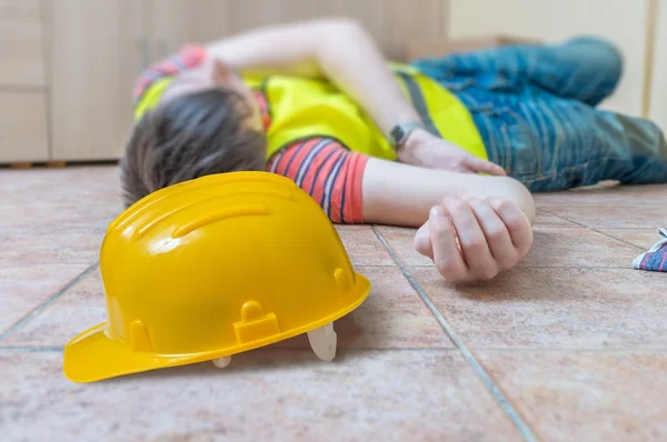 O trabalhador ferido teve um acidente. O homem está deitado no chão. Capacete amarelo na frente . — Fotografia de Stock