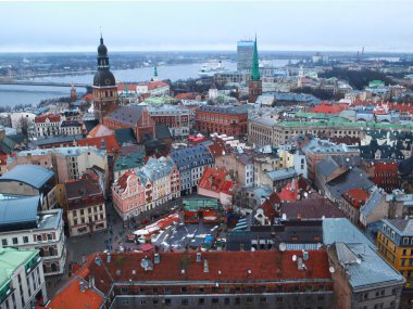 Kiremit kaplı çatılar, insanlarla dolu sokaklar ve park edilmiş arabalar. Riga, Letonya