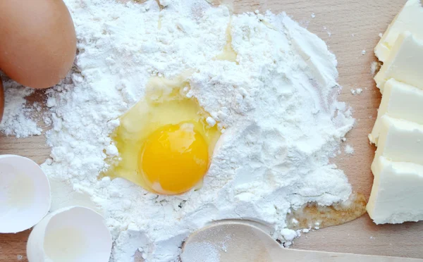 White flour with eggs, butter and wooden spoon on a cooking board — Stock Photo, Image