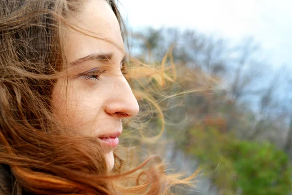 Jeune belle femme aux cheveux longs flottant dans le vent sourit et regarde l'horizon en pensant — Photo