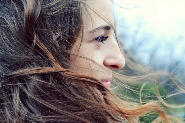 Jeune belle femme aux cheveux longs flottant dans le vent sourit et regarde l'horizon en pensant — Photo