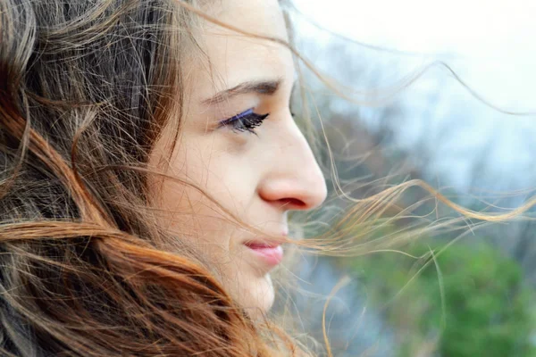Jeune belle femme aux cheveux longs flottant dans le vent sourit et regarde l'horizon en pensant — Photo