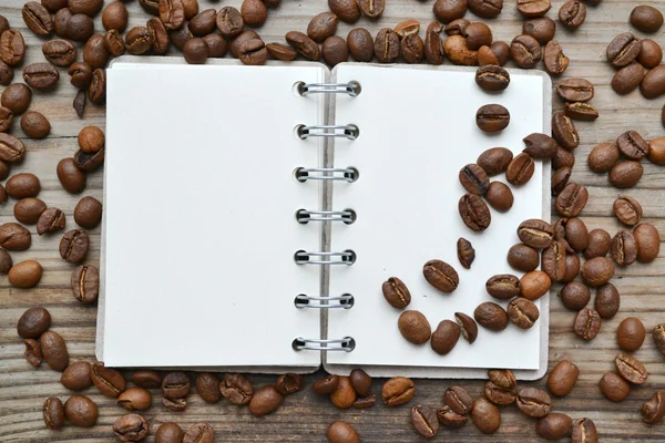 An empty retro spiral notebook with lots of roasted coffee beans — Stock Photo, Image