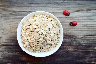 Ahşap masa üzerinde beyaz kase çiğ yulaf gevreği