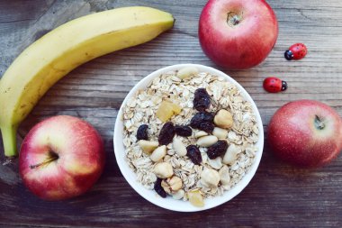 Çiğ yulaf gevreği ile fındık ve ahşap masa üzerinde beyaz kase kuru üzüm