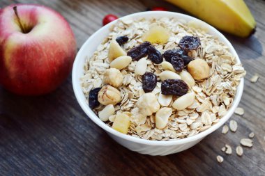 Çiğ yulaf gevreği ile fındık ve ahşap masa üzerinde beyaz kase kuru üzüm