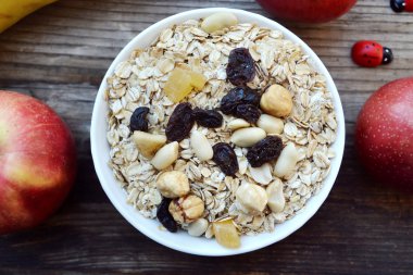 Çiğ yulaf gevreği ile fındık ve ahşap masa üzerinde beyaz kase kuru üzüm