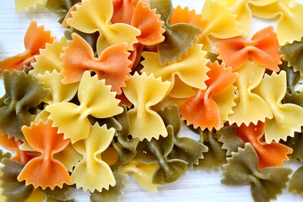 Uncooked butterfly shaped colorful pasta farfalle on wooden table — Stock Photo, Image