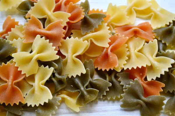 Uncooked butterfly shaped colorful pasta farfalle on wooden table — Stock Photo, Image