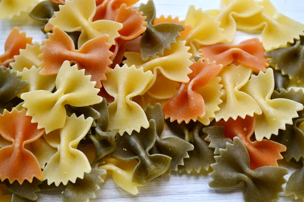 Borboleta não cozida em forma de farfalle de macarrão colorido na mesa de madeira — Fotografia de Stock