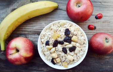 Çiğ yulaf gevreği ile fındık ve ahşap masa üzerinde beyaz kase kuru üzüm