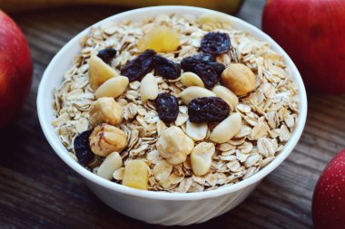 Çiğ yulaf gevreği ile fındık ve ahşap masa üzerinde beyaz kase kuru üzüm