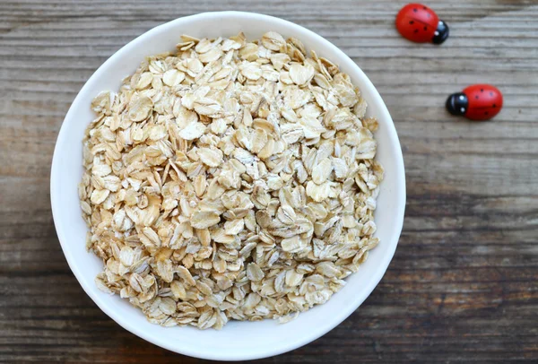 Copos de avena crudos en tazón blanco sobre mesa de madera — Foto de Stock