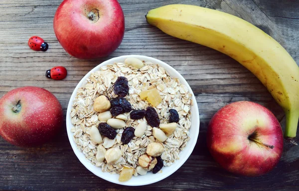 Çiğ yulaf gevreği ile fındık ve ahşap masa üzerinde beyaz kase kuru üzüm