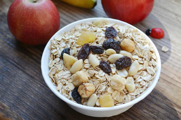 Flocons d'avoine crus avec noix et raisins secs dans un bol blanc sur une table en bois — Photo