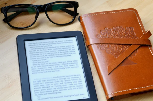 Black ereader with reading glasses and an old notebook in leather cover on wooden table — Stock Photo, Image
