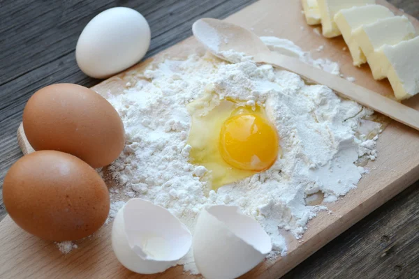 Farina bianca con uova, burro e cucchiaio di legno su un piano di cottura — Foto Stock