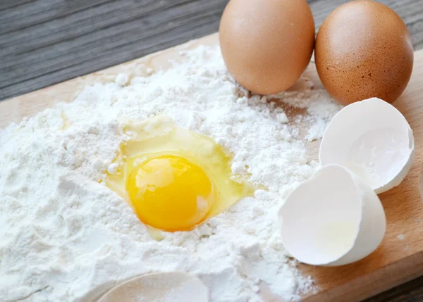 White flour with eggs, butter and wooden spoon on a cooking board — Stock Photo, Image