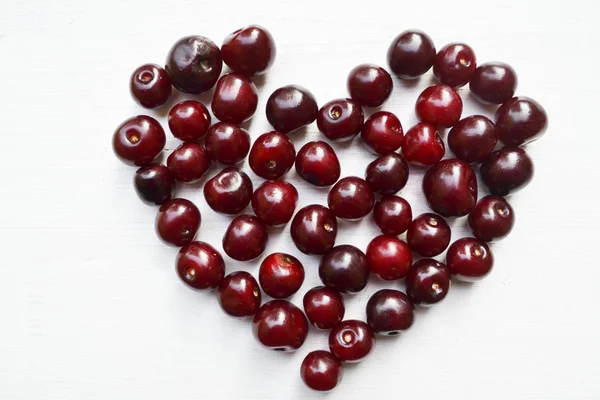 Lots of fresh and tasty dark sweet cherries in shape of heart isolated on white — Stock Photo, Image