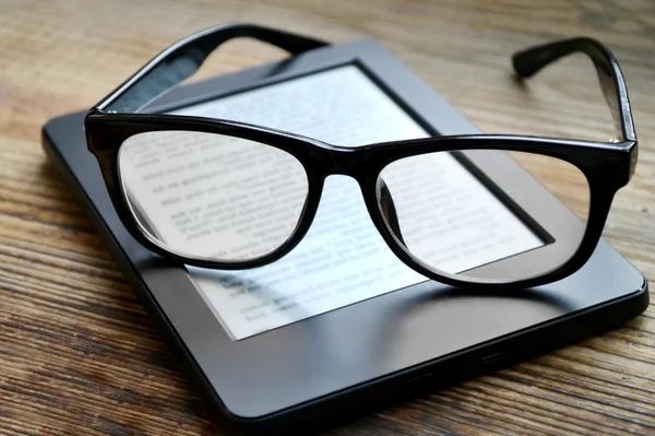 Black ereader with retro glasses on wooden table — Stock Photo, Image