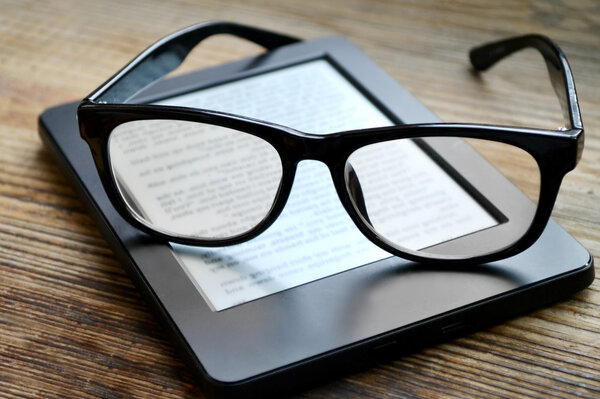 Black ereader with retro glasses on wooden table