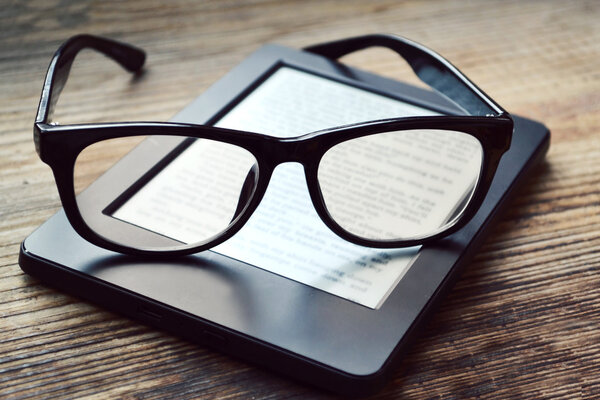 Black ereader with retro glasses on wooden table