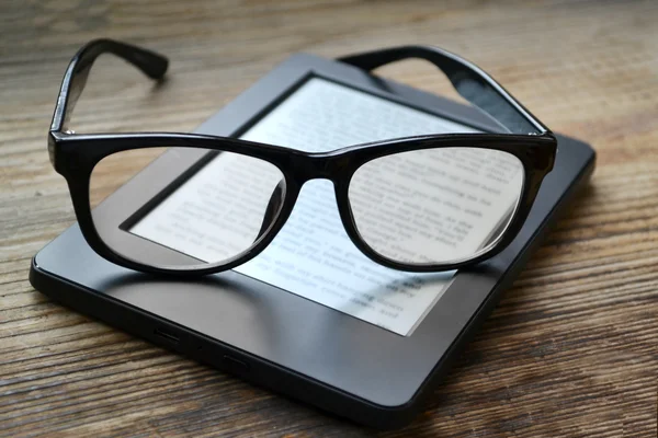 Black ereader with retro glasses on wooden table — Stock Photo, Image