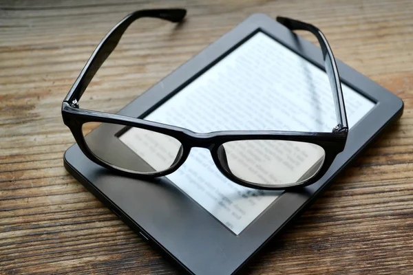 Black ereader with retro glasses on wooden table — Stock Photo, Image